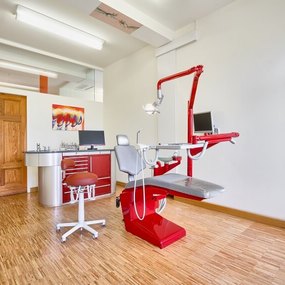 Moderner Zahnarztpraxisraum mit rotem Behandlungsstuhl und zahnärztlicher Ausstattung.